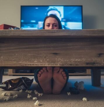 Romantic Movies That’ll Melt Even the Coldest Heart Person crying under a coffee table, feet and popcorn visible.